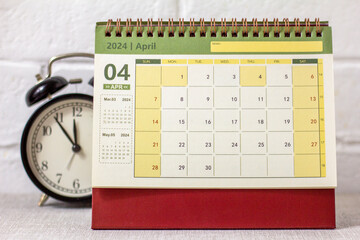 Desk calendar for April 2024 and a clock on the table. - obrazy, fototapety, plakaty