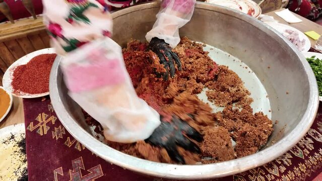 A female chef is kneading a cig kofte traditional Turkish raw meatball in a copper tray during traditional Sira Night.