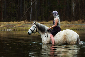 young woman with white hair riding water on a white horse