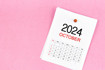 October 2024 calendar page and wooden push pin on pink background.