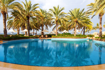 Fototapeta na wymiar Swimming pool with clear water surrounded by palm trees in one of the best resorts