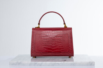 Red color, luxury fashion handbag made of crocodile skin, on marble and white background