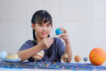 Young Asian girl Making Solar system Model on wooden table at home for her Science Homework project...
