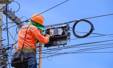 Technician on ladder is Repairing Fiber Optic Cable in Internet Splitter Box on Electric Pole against blue sky background