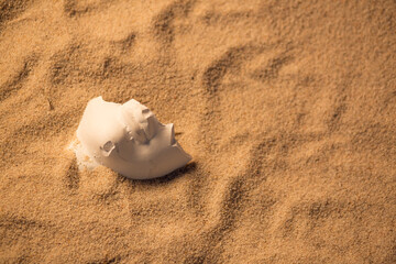 A fragment of a plaster sculpture in the sand. Lower part of the face.