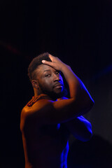 Studio portrait of a young man with a naked torso with blue-red backlighting on a black background.