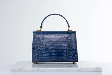 Foto auf Alu-Dibond Luxury fashionable navy blue color crocodile skin bag on marble and white background in studio © Cumhur