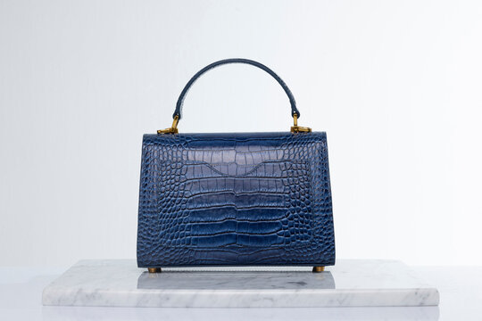 Luxury fashionable navy blue color crocodile skin bag on marble and white background in studio