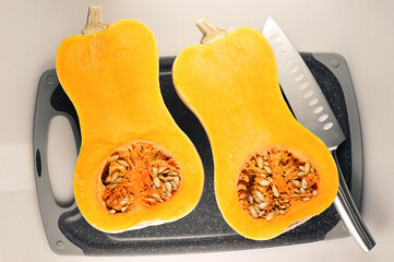 a pumpkin cut in half on a board and a knife