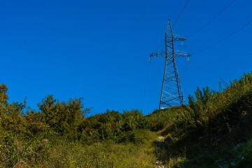 Obraz premium High-voltage power transmission line support against a background of blue sky in the forested mountains of the Western Caucasus on a sunny summer day