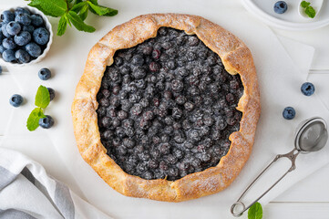 Blueberry galette, open pie or tart with ice cream and cup of tea on a white wooden table. Summer...