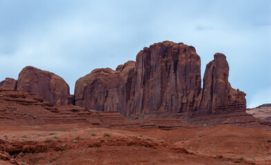Fototapeta premium Desert landscape with red rocks and dry vegetation on red sands in Monument Valley, Navajo Nation, Arizona - Utah