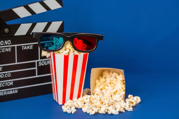 A banner for the film industry. A romantic movie date. A movie camera, 3D glasses, popcorn in striped cups on a blue background. The premiere of the film.