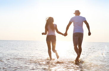 Happy young couple having fun running on beach at sunset