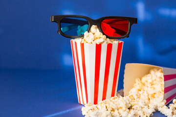 A banner for the film industry. A romantic movie date. A movie camera, 3D glasses, popcorn in striped cups on a blue background. The premiere of the film.