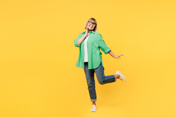 Fototapeta na wymiar Full body side profile view happy elderly blonde woman 50s year old wear green shirt glasses casual clothes put hand on face raise up leg isolated on plain yellow background studio. Lifestyle concept.