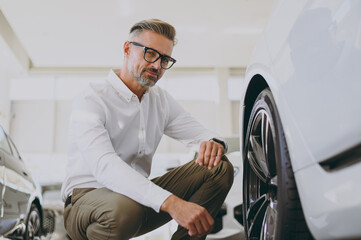 Close up adult rich man customer male buyer client wear shirt check touch wheel rim tire choose auto want to buy new automobile in car showroom vehicle salon dealership store motor show Sales concept