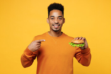 Young man wear orange sweatshirt casual clothes point index finger on burger isolated on plain...