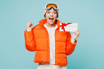 Skier winner young woman wear padded windbreaker jacket hat ski goggles mask hold store gift coupon voucher card travel rest spend weekend winter season in mountains isolated on plain blue background. © ViDi Studio