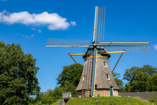 Selective focus of rooftop and blade of windmill, Traditional Dutch windmill on green grass meadow under blue sky and white puffy clouds, Summer landscape view in countryside of Netherlands.