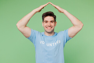 Fototapeta premium Young man he wear blue t-shirt white title volunteer hold folded hands above head like house roof isolated on plain pastel green background. Voluntary free work assistance help charity grace concept.