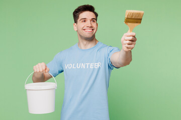 Young smiling happy man wear blue t-shirt white title volunteer hold paint brush bucket work...