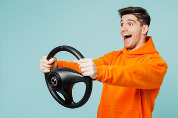 Side view excited surprised young man he wears orange hoody casual clothes hold steering wheel...