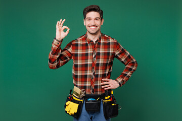 Young confident fun employee laborer handyman man wear red shirt showing okay ok gesture isolated...
