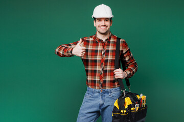 Young smiling employee laborer handyman man wear red shirt hardhat hold bag with tools show thumb...