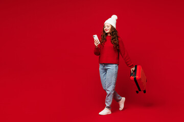 Traveler woman wear sweater hat casual clothes hold bag use mobile cell phone isolated on plain red color background. Tourist travel abroad in free time rest getaway. Air flight trip journey concept. - obrazy, fototapety, plakaty