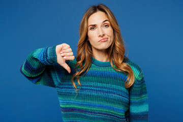 Young sad dissatisfied woman she wearing knitted sweater casual clothes showing thumb down dislike gesture look camera isolated on plain blue cyan color background studio portrait. Lifestyle concept.