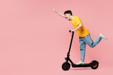 Full body side profile view student happy young man he wears yellow t-shirt casual clothes driving electric scooter isolated on plain pastel light pink background studio portrait. Lifestyle concept. © ViDi Studio