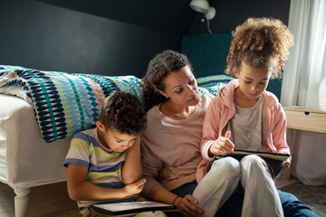Carefree mother with children using tablets on bedroom floor