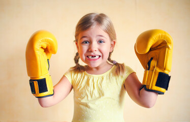 Little girl with yellow boxing gloves over yellow wall background. Girl power concept