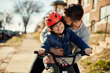 Father teaching child to ride a bicycle in suburb - obrazy, fototapety, plakaty