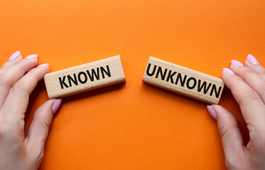 Known or Unknown symbol. Concept word Known or Unknown on wooden blocks. Businessman hand. Beautiful orange background. Business and Known or Unknown concept. Copy space