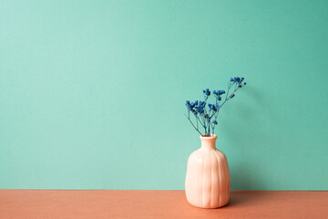 Vase of dry blue gypsophila flower on red table. mint green wall background