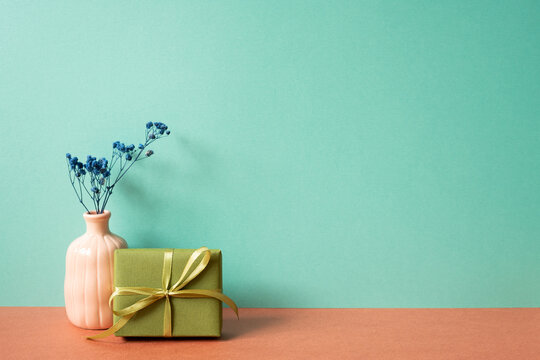 Khaki gift box with vase of dry flower on red table. mint green wall background - Powered by Adobe
