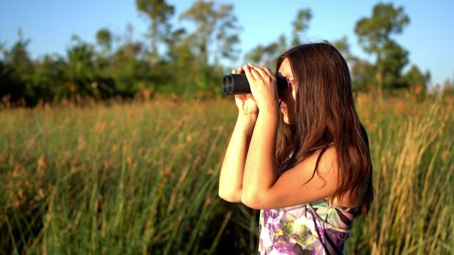 Young brunette woman looking through her binoculars outdoors on a sunny day.