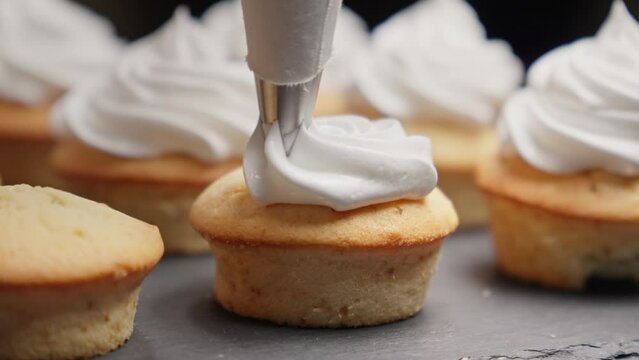 Confectioner putting Italian meringue cream on tasty muffins. Cupcakes with vanilla cream. Making muffins for party. Decorating cup-cake with cream. Close-up in 4K, UHD