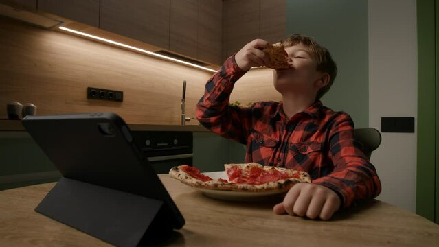 kid relishes a tasty pizza slice while engrossed in a tablet computer. Perfect for portraying the modern blend of tech and mealtime enjoyment