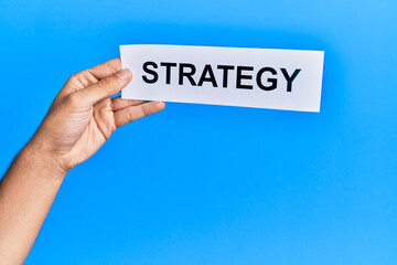 Hand of caucasian man holding paper with strategy word over isolated blue background
