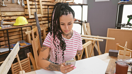 Armless hispanic carpenter woman leverages technology, uses smartphone in her woodwork workshop