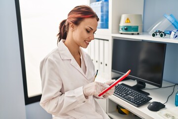 Young caucasian woman scientist smiling confident using touchpad at laboratory