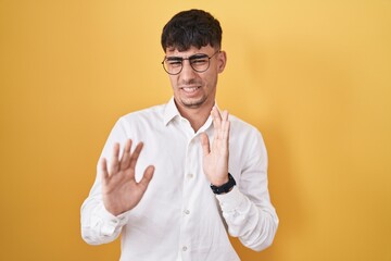 Young hispanic man standing over yellow background disgusted expression, displeased and fearful...