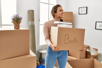 Young beautiful hispanic woman smiling confident holding books package at new home