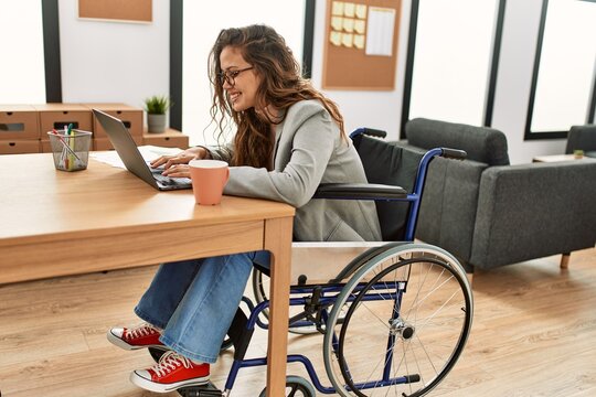 Young beautiful hispanic woman business worker using laptop sitting on wheelchair at office