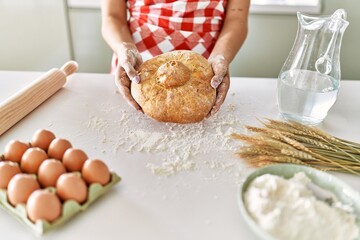 Young beautiful hispanic woman holding bread at the kitchen