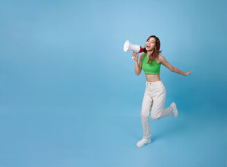 Young Asian teen woman running and hand holding megaphone announce discount isolated on blue copy...