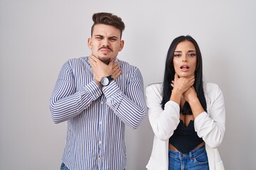 Young hispanic couple standing over white background shouting suffocate because painful strangle. health problem. asphyxiate and suicide concept.